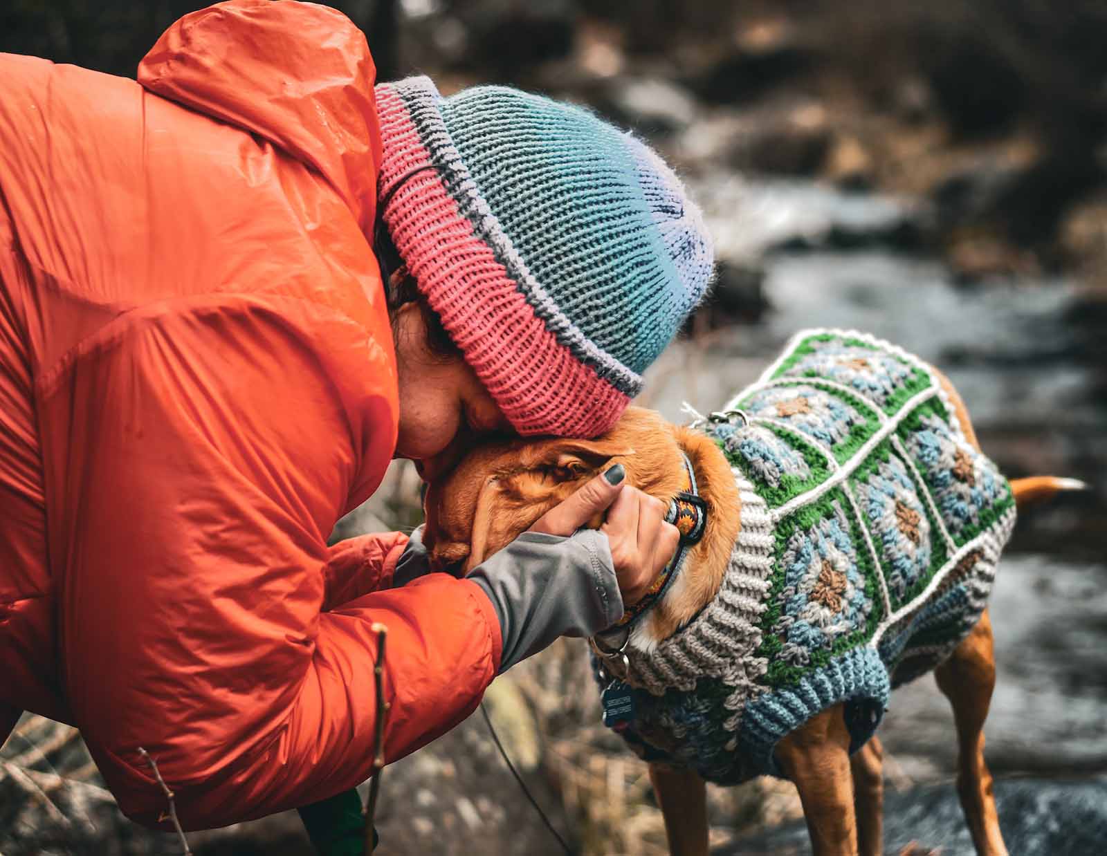 A lady hugging her dog, they are both wearing knitting gear like hats and sweater
